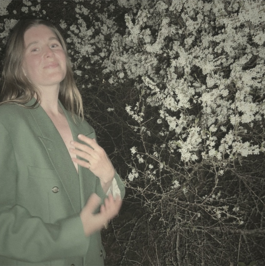 Polaroid-style photo of Elenore in a green blazer among spring blossoms